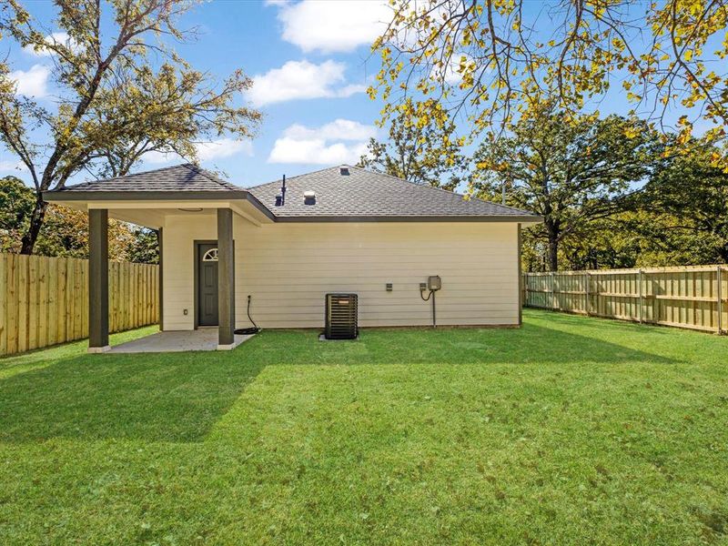 Rear view of property featuring a fenced backyard, a shingled roof, and a patio area
