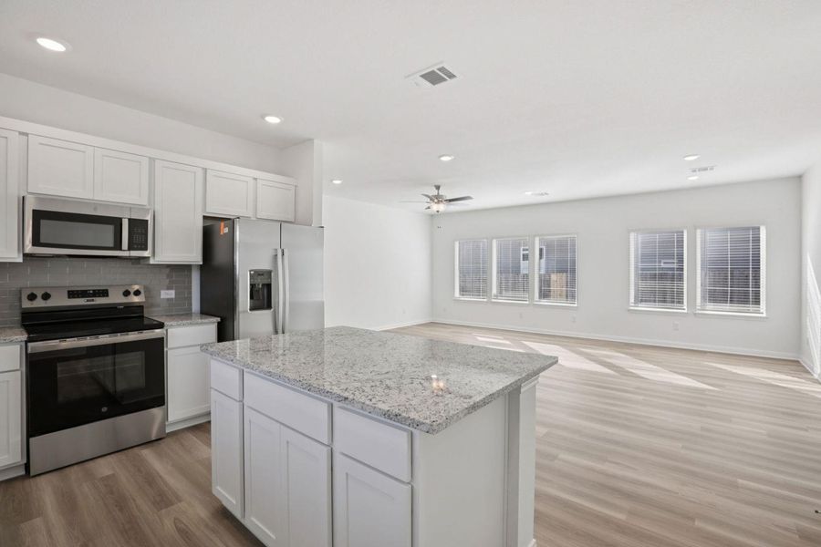 Kitchen with stainless steel appliances, a center island, white cabinetry, light wood-type flooring, and open floor plan
