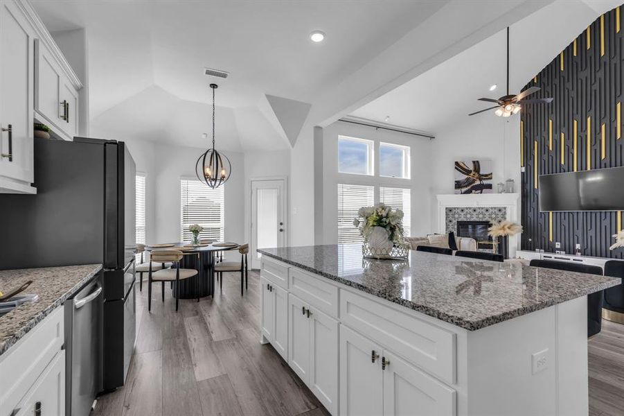 Kitchen featuring light hardwood / wood-style flooring, a kitchen island, ceiling fan with notable chandelier, white cabinetry, and a tiled fireplace