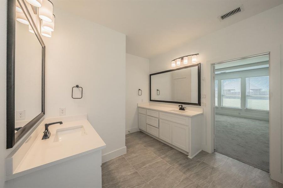 Primary bathroom features two white vanities with integrated sinks and dark-toned faucets, complemented by two framed mirrors and overhead lighting