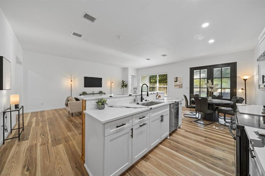 Kitchen with dishwasher, sink, white cabinetry, light hardwood / wood-style flooring, and wall chimney range hood