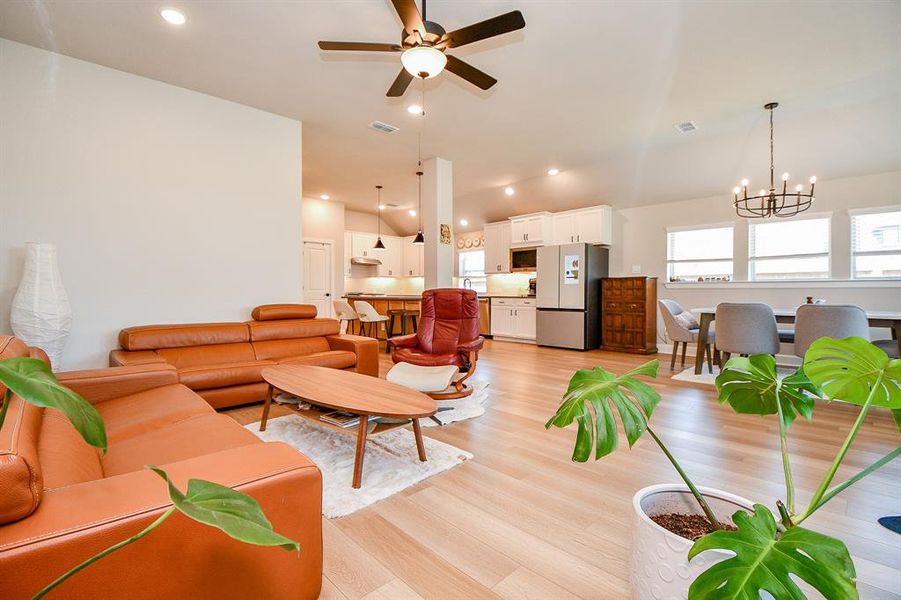 Bright and open living area with modern design. Features include hardwood floors, a cozy leather sofa, ceiling fan, and ample natural light. The kitchen and dining space are seamlessly integrated, offering a welcoming atmosphere for entertaining.