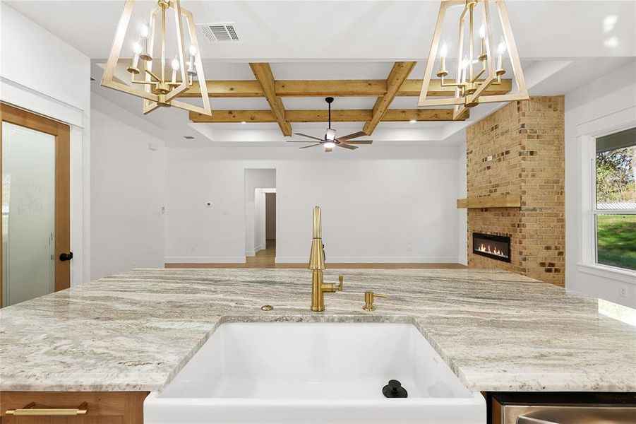 Kitchen with a chandelier, coffered ceiling, beamed ceiling, a brick fireplace, and light stone counters