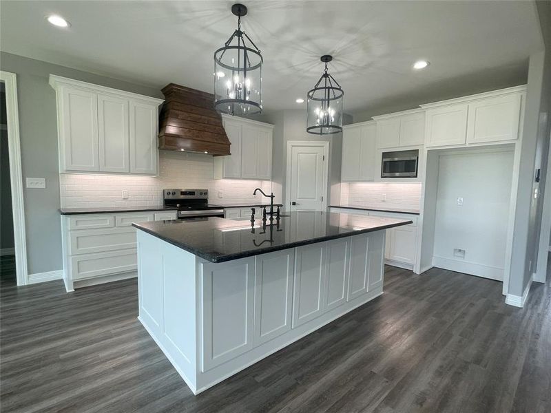 Kitchen with premium range hood, white cabinetry, appliances with stainless steel finishes, backsplash, and hanging light fixtures