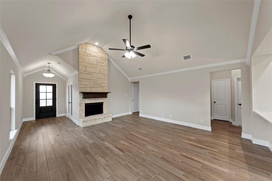 Spacious living area featuring vaulted ceilings, a stone-clad fireplace with a wood mantel, and wood-finish flooring