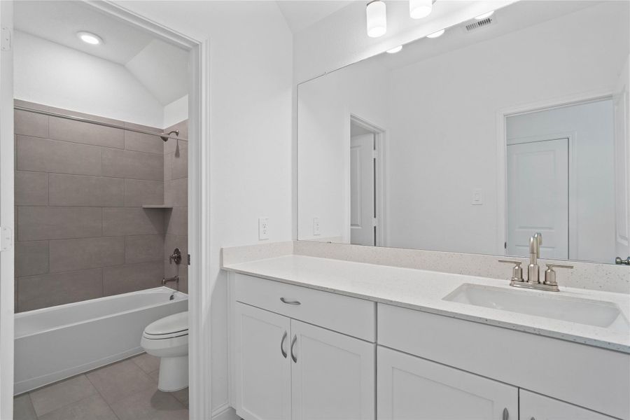 Secondary bathroom featuring an extended vanity cabinet with single bowl sink, brushed nickel hardware, mirror and vanity lighting, tub/shower combination with tile surround and tile flooring.