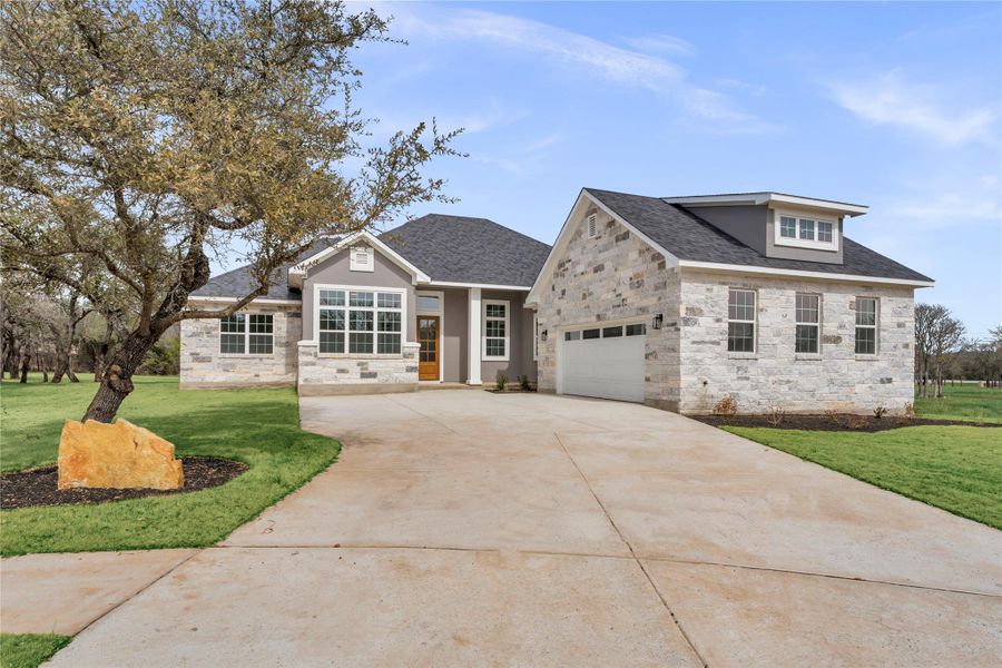 View of front of home featuring stone siding, a front lawn, and driveway