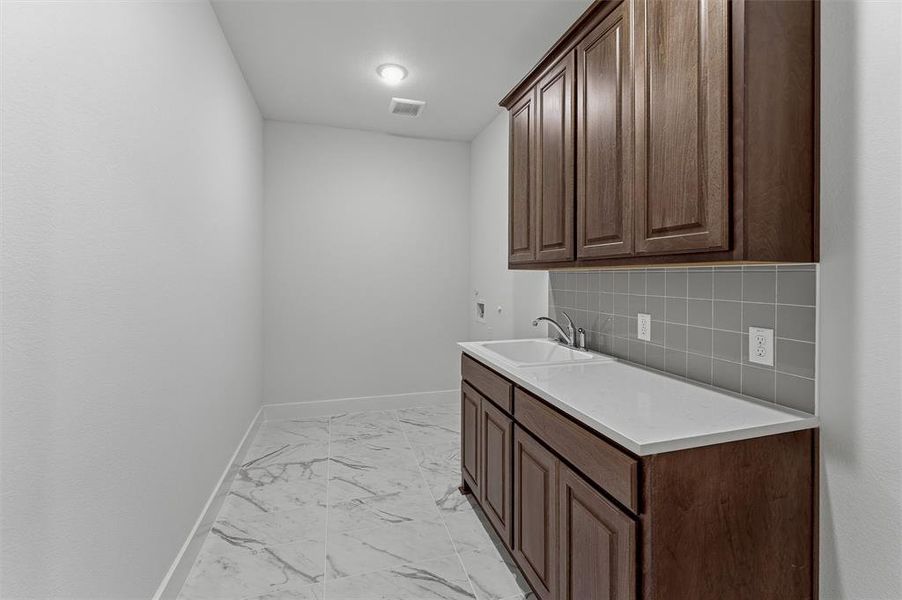 Laundry room featuring dark wood-finish cabinetry, a white countertop with an integrated sink, and gray subway tile backsplash Laundry room featuring dark wood-finish cabinetry, a white countertop with an integrated sink, and gray subway tile backsplash