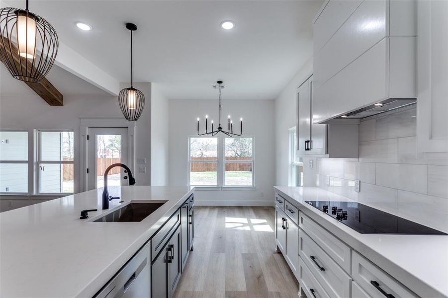 Kitchen with black electric stovetop, premium range hood, a sink, light countertops, and decorative backsplash