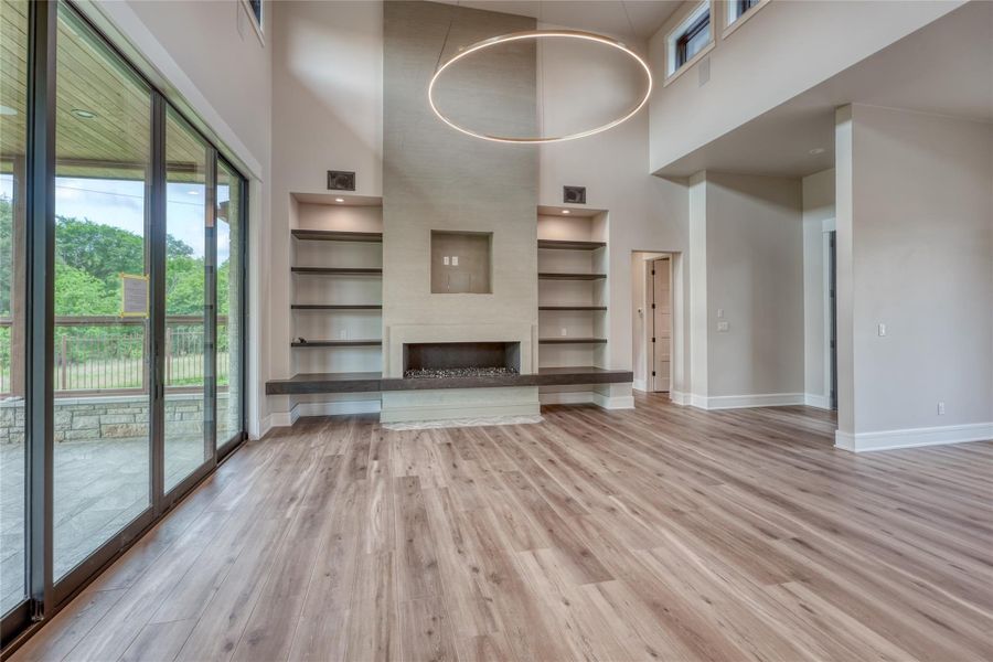 Unfurnished living room featuring a towering ceiling, built in features, baseboards, wood finished floors, and a fireplace