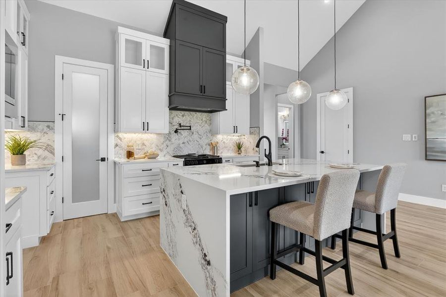 Kitchen featuring a waterfall-edge island with seating, a gas range with a pot filler, a two-tone cabinetry scheme, and recessed under-cabinet lighting