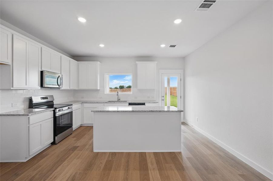 Kitchen featuring appliances with stainless steel finishes, a sink, a center island, light stone counters, and light wood-style flooring Kitchen featuring appliances with stainless steel finishes, a sink, a center island, light stone counters, and light wood-style flooring