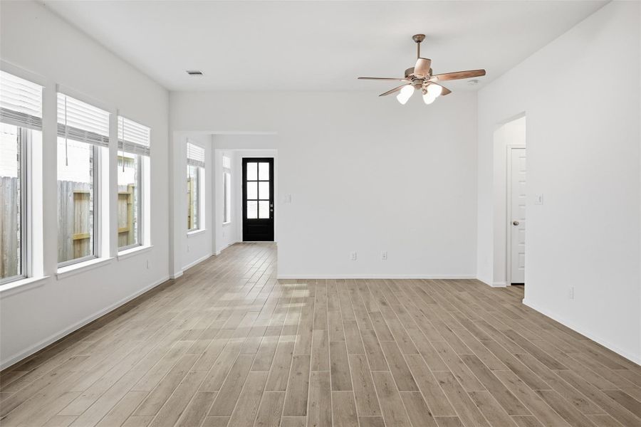 Bright and spacious living area with abundant natural light from large windows, featuring elegant wood-look tile flooring and a stylish ceiling fan.
