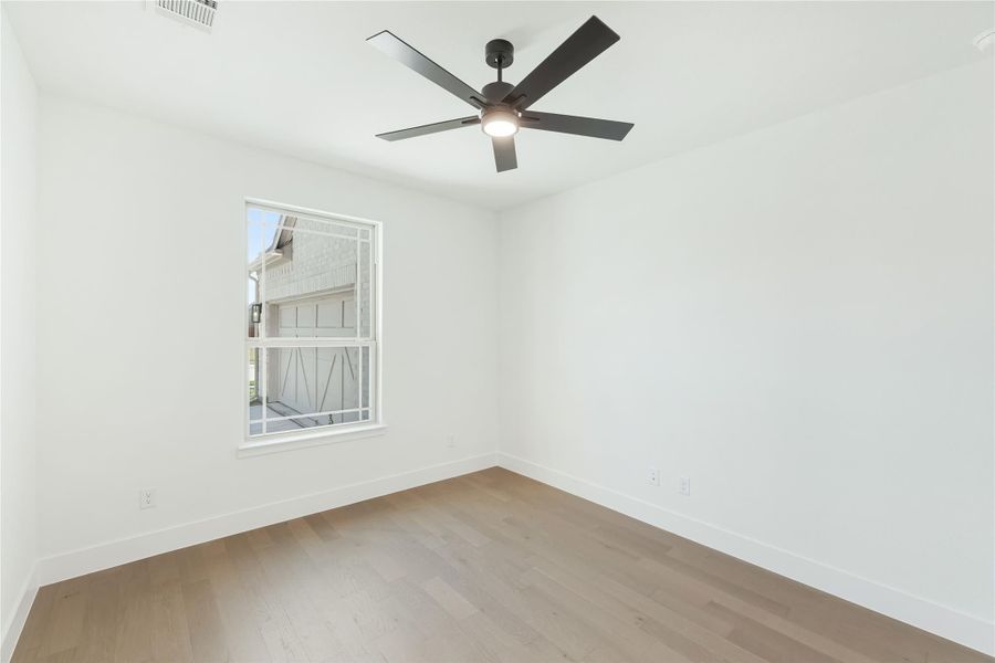 Empty bedroom with white walls, light hardwood floors, ceiling fan, and single window
