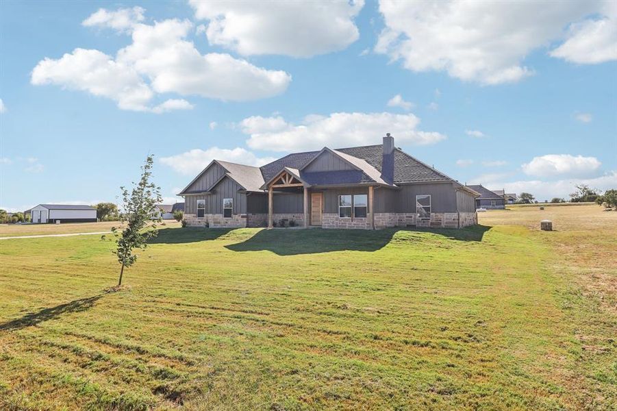 Rear view of house featuring stone siding, a lawn, a chimney, and board and batten siding Rear view of house featuring stone siding, a lawn, a chimney, and board and batten siding