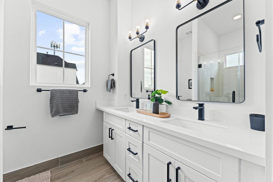 This elegant primary bathroom features a sleek double-sink vanity topped with quartz countertops, offering both style and functionality. The spacious layout includes a glass-enclosed walk-in shower, accented with modern tilework and premium fixtures.