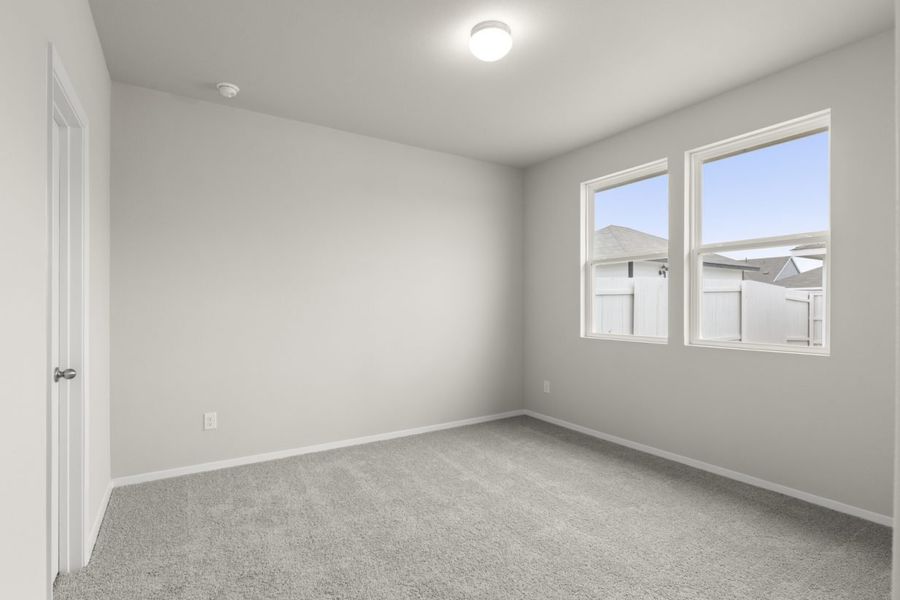 Image of a primary bedroom with cream walls, tan carpeting, white trim and two windows