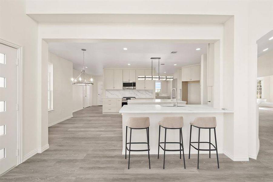 Kitchen with pendant lighting, a kitchen bar, stainless steel appliances, light wood-type flooring, and light stone counters Kitchen with pendant lighting, a kitchen bar, stainless steel appliances, light wood-type flooring, and light stone counters