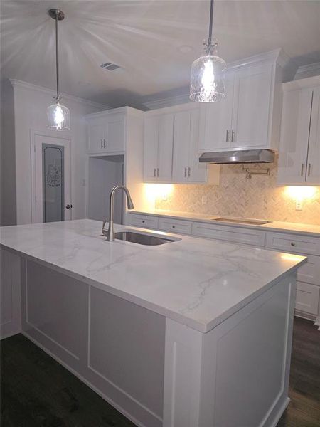 Kitchen with white cabinets, dark wood-style flooring, light stone counters, hanging light fixtures, and ornamental molding Kitchen with white cabinets, dark wood-style flooring, light stone counters, hanging light fixtures, and ornamental molding