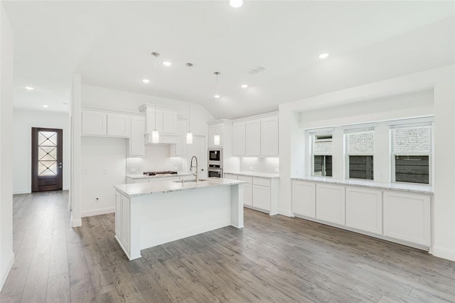 Open kitchen with white cabinets, large island, granite countertops, and hardwood floors Open kitchen with white cabinets, large island, granite countertops, and hardwood floors