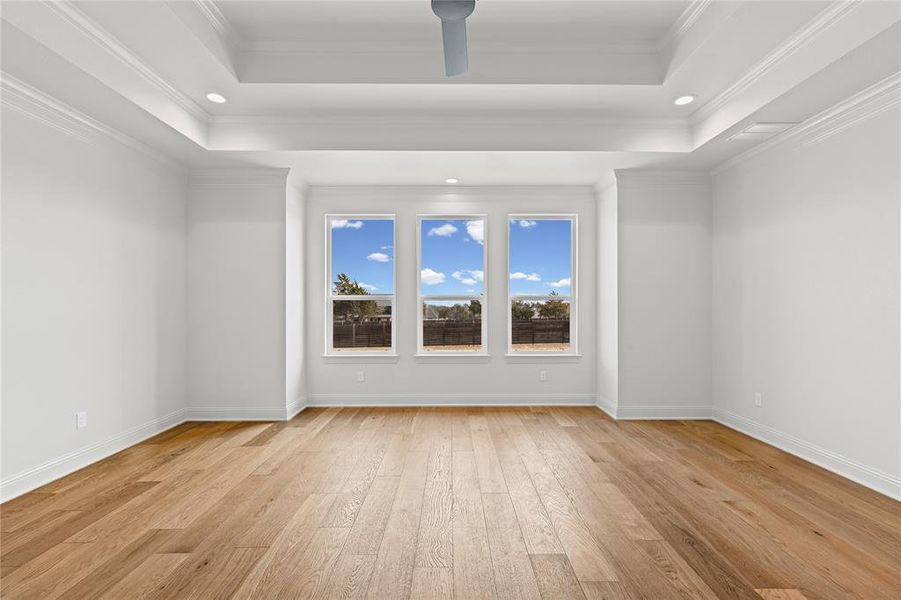 Spare room with light wood-style floors, recessed lighting, ornamental molding, and a tray ceiling