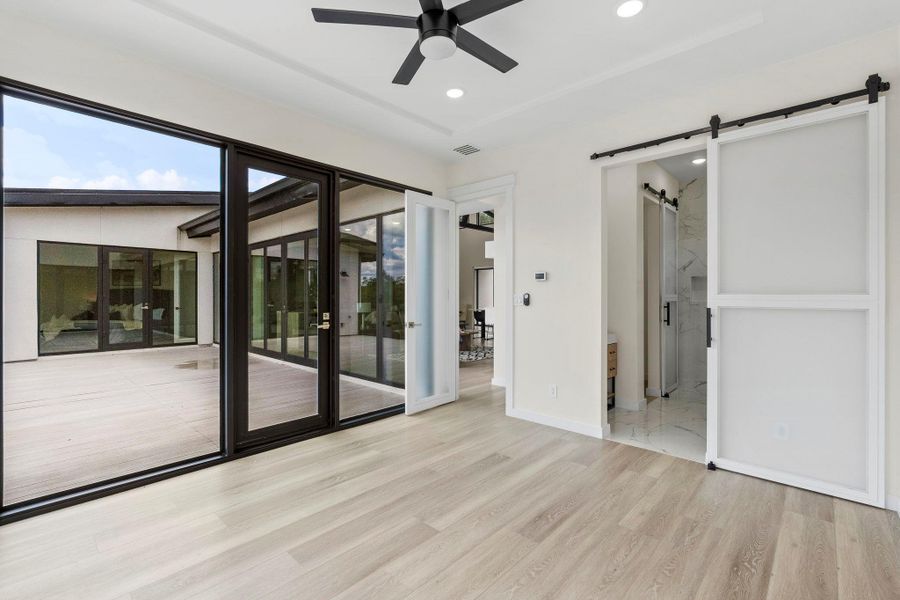 Unfurnished bedroom with a barn door, access to outside, light wood-type flooring, ceiling fan, and connected bathroom