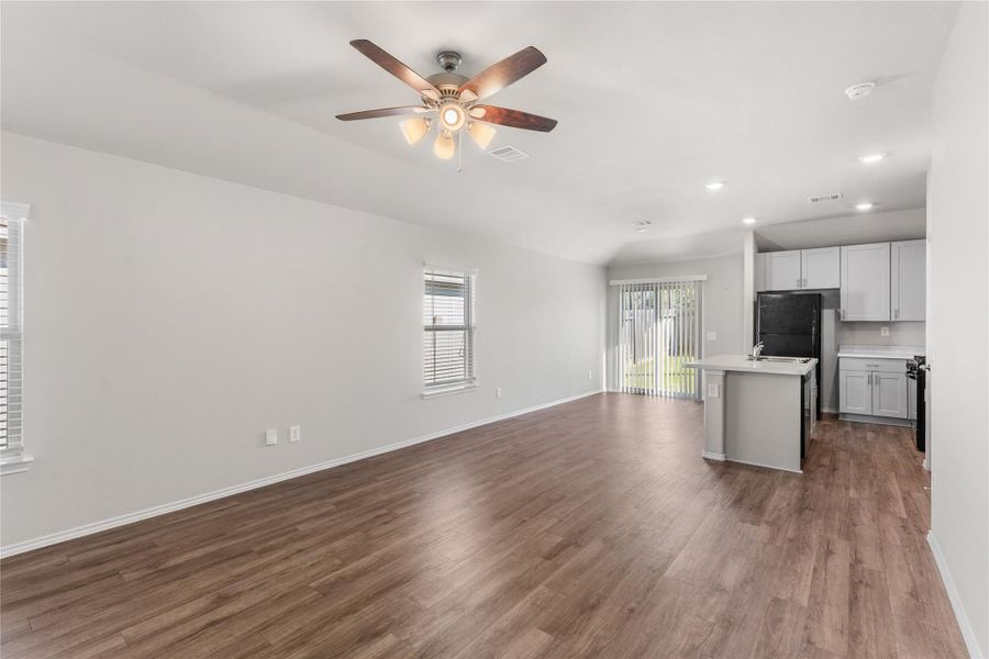 Open-concept living area with wood-style flooring and ceiling fan. Open-concept living area with wood-style flooring and ceiling fan.