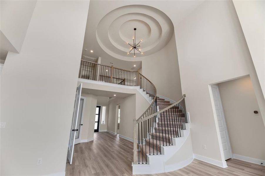 Entrance foyer featuring a chandelier, light wood finished floors, a towering ceiling, and stairs