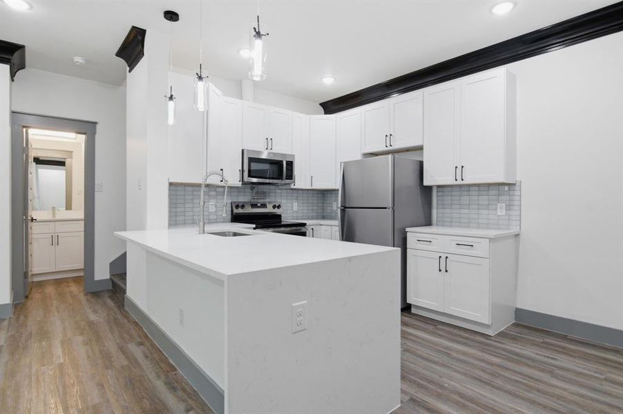 Open-concept kitchen featuring white shaker cabinetry, stainless steel appliances, a center island with an undermount sink, and wood-finish flooring