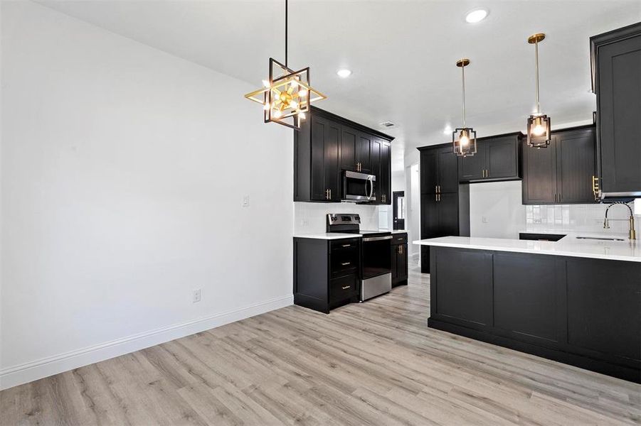 Kitchen featuring appliances with stainless steel finishes, light hardwood / wood-style flooring, tasteful backsplash, pendant lighting, and kitchen peninsula