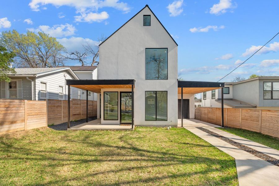 Rear view of property featuring an attached carport, driveway, a yard, stucco siding, and fence private yard