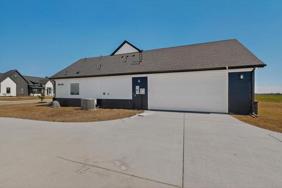 View of side of home featuring concrete driveway, a shingled roof, and a garage