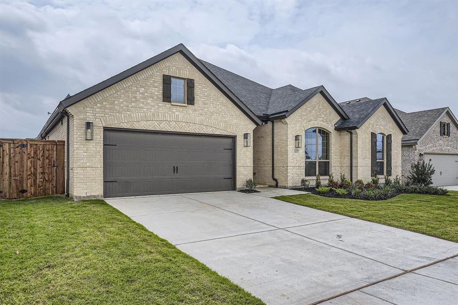French country inspired facade with brick siding, concrete driveway, a garage, and roof with shingles