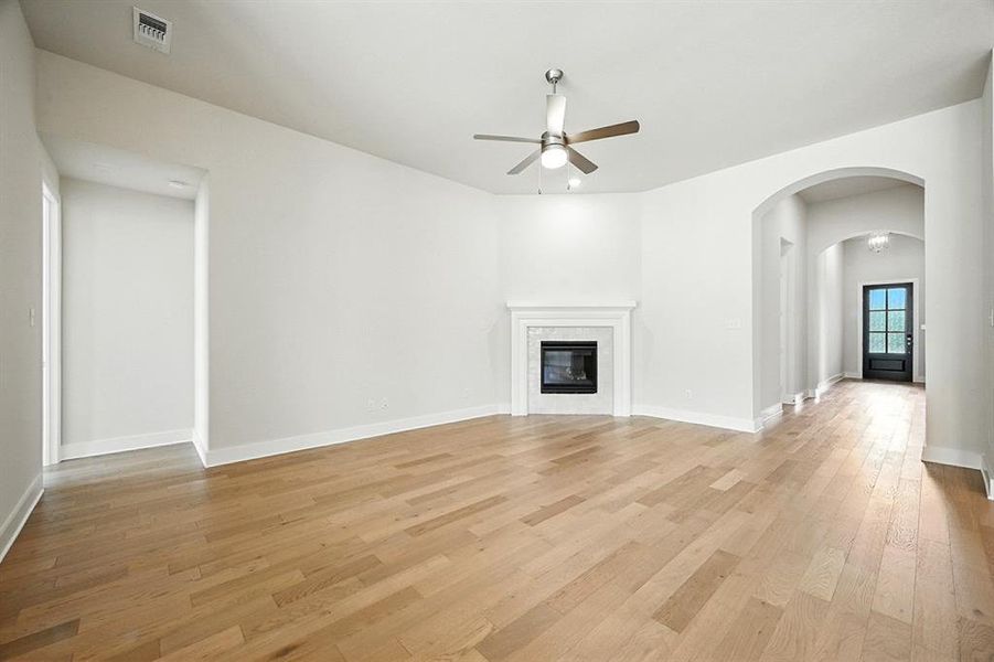 Unfurnished living room featuring light wood-style flooring, a glass covered fireplace, arched walkways, and a ceiling fan Unfurnished living room featuring light wood-style flooring, a glass covered fireplace, arched walkways, and a ceiling fan