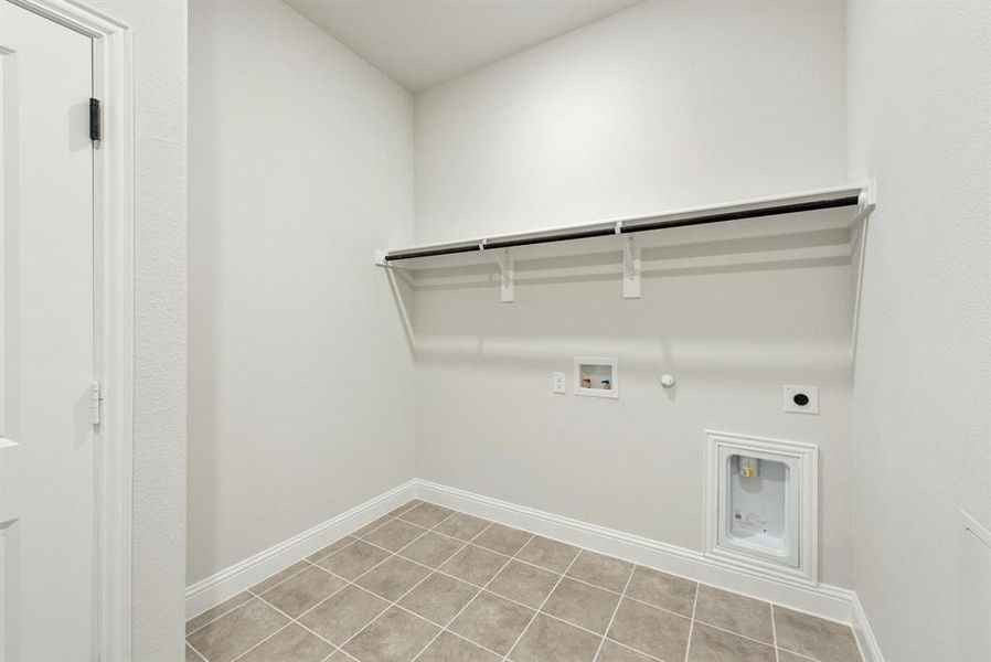 Dedicated utility space featuring neutral-toned tile flooring, white baseboards, and a white door with black hinges Dedicated utility space featuring neutral-toned tile flooring, white baseboards, and a white door with black hinges