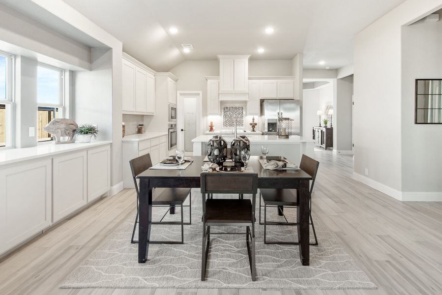 Open dining area with dark wood table and chairs, flowing into white kitchen with island and light hardwood floors
