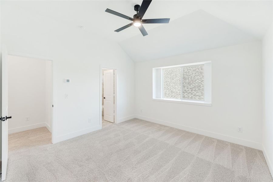 Empty bedroom with vaulted ceiling, ceiling fan, carpet flooring, and a window