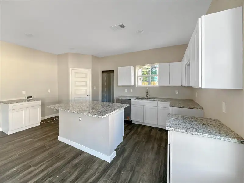 Kitchen with light stone counters, a center island, white cabinetry, and dark wood-style floors