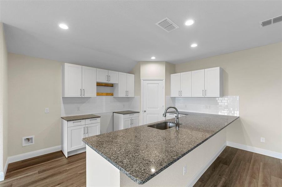 Modern kitchen featuring a large island with an undermount sink, granite countertops, white shaker cabinetry, white subway tile backsplash, and wood-finish flooring