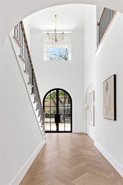 Foyer featuring arched walkways, french doors, stairs, a towering ceiling, and a chandelier Foyer featuring arched walkways, french doors, stairs, a towering ceiling, and a chandelier