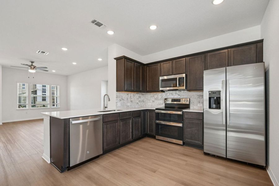 Kitchen featuring stainless steel appliances, dark brown cabinets, recessed lighting, decorative backsplash, and open floor plan