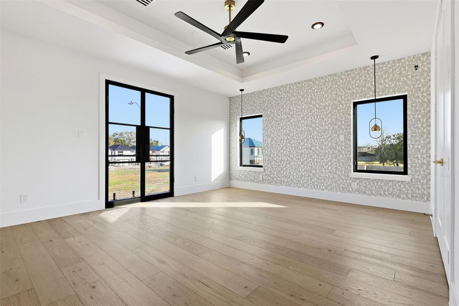 Same floorplan - different finishes. The Primary Bedroom includes a tray ceiling with a modern fan, a geometric accent wall, and direct access to a private outdoor balcony.