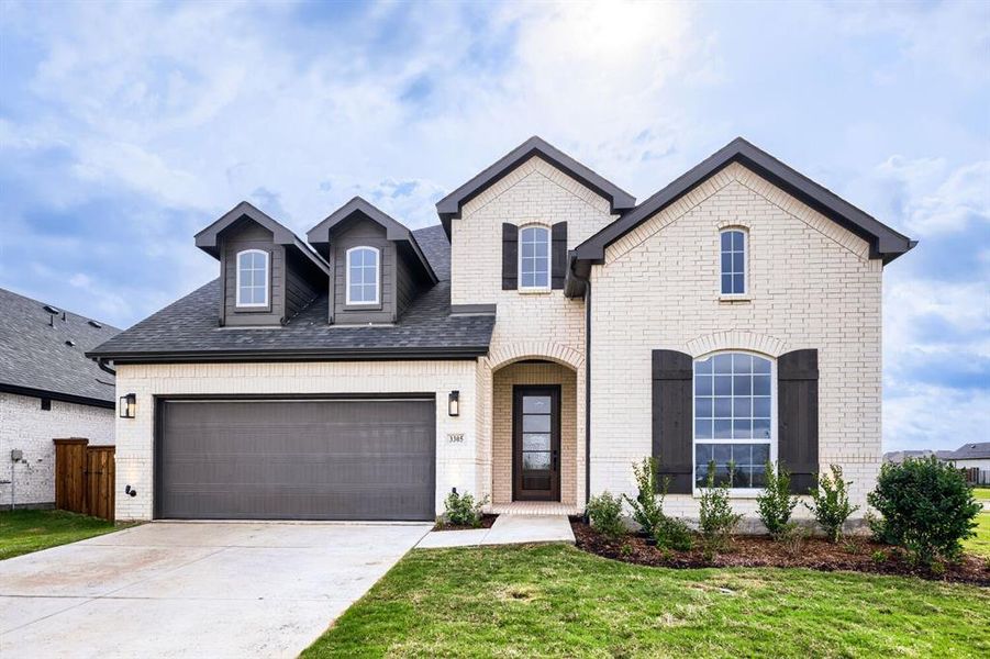 French country inspired facade with concrete driveway, brick siding, a front yard, and a shingled roof