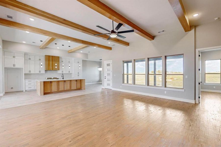 Unfurnished living room with ceiling fan, sink, light wood-type flooring, and beam ceiling