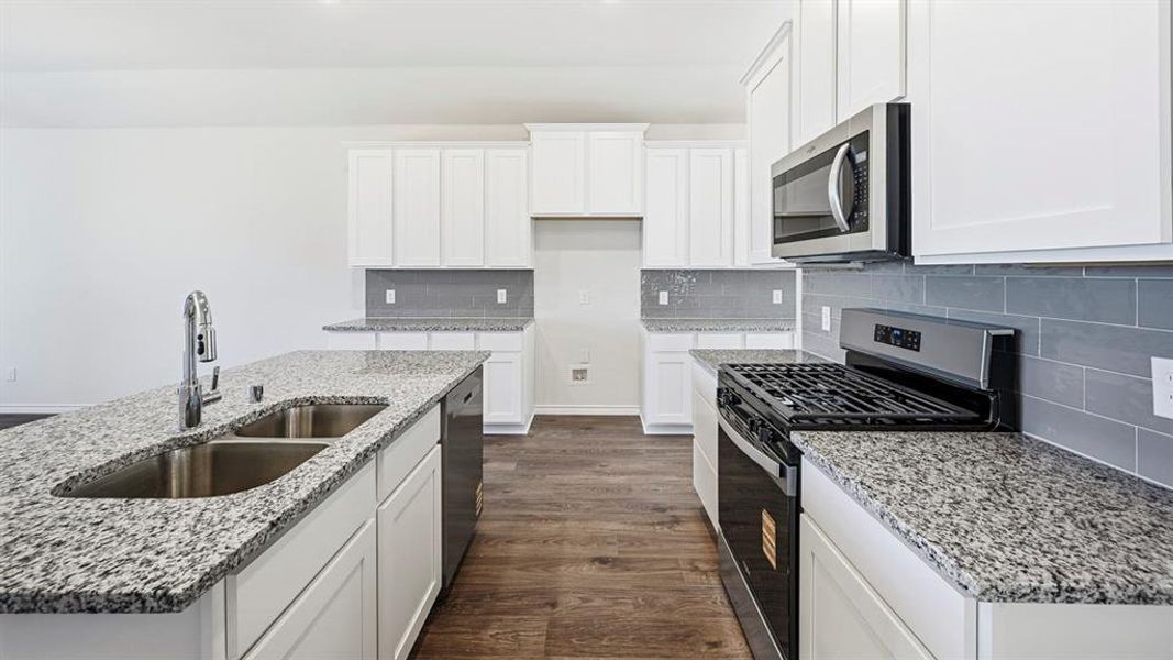 Kitchen with appliances with stainless steel finishes, dark wood-type flooring, white cabinetry, and light stone countertops