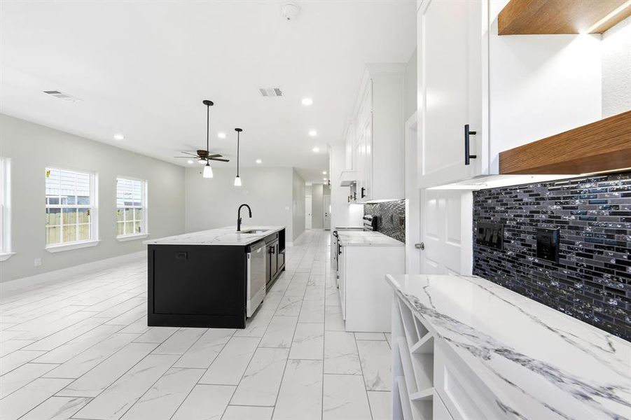 Dual tone kitchen featuring decorative backsplash, two tone color scheme, an island with sink, hanging light fixtures, and a ceiling fan