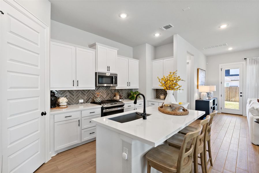 Kitchen with white cabinets, a center island with sink, a breakfast bar area, light wood finished floors, and recessed lighting