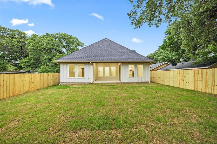 Spacious backyard featuring a newly installed wooden privacy fence, a concrete patio, and a white siding exterior with multiple windows