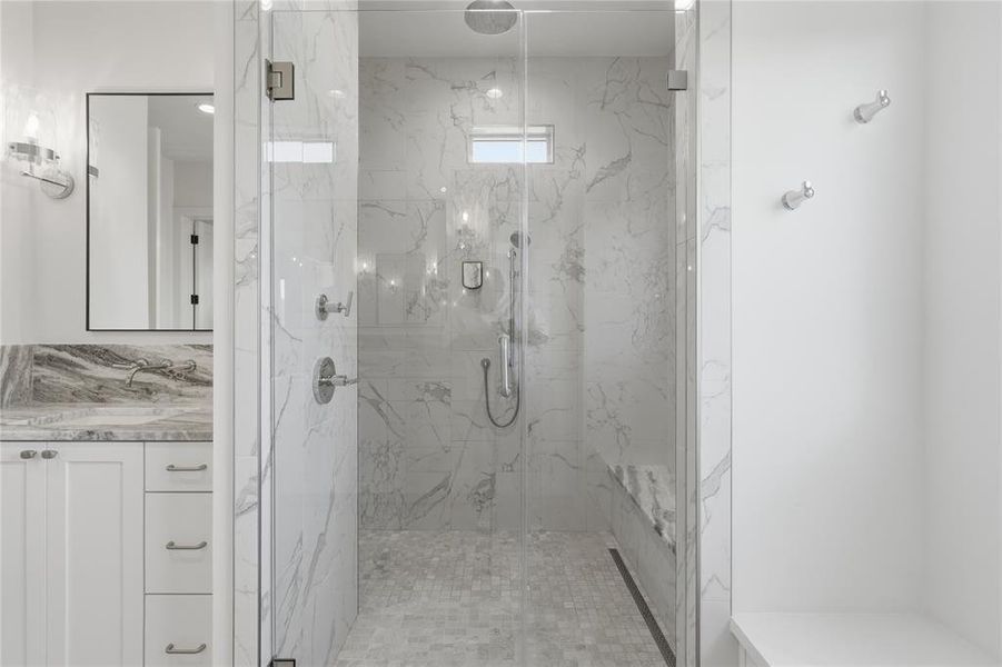 Frameless glass shower enclosure featuring a rain shower head, hand-held shower, and built-in bench