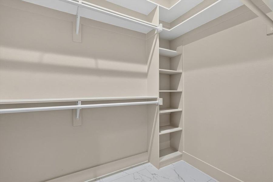 Closet featuring white shelving, multiple hanging rods, built-in vertical storage, light neutral wall tones, and marble-look tile flooring